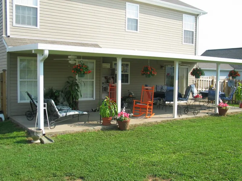 Long patio cover across the back of a two-story home, with rocking chairs and hanging plants