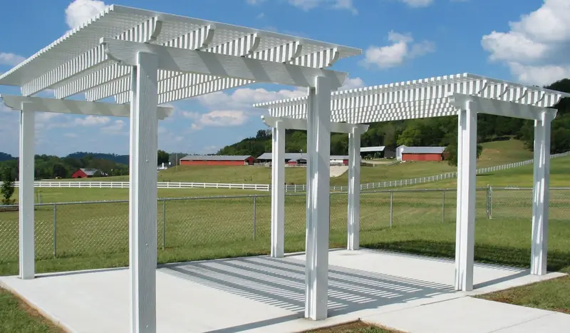 Freestanding white pergola on a concrete pad with farmland behind it