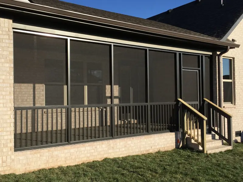 Dark-framed screen room with railing and steps on the back of a brick home