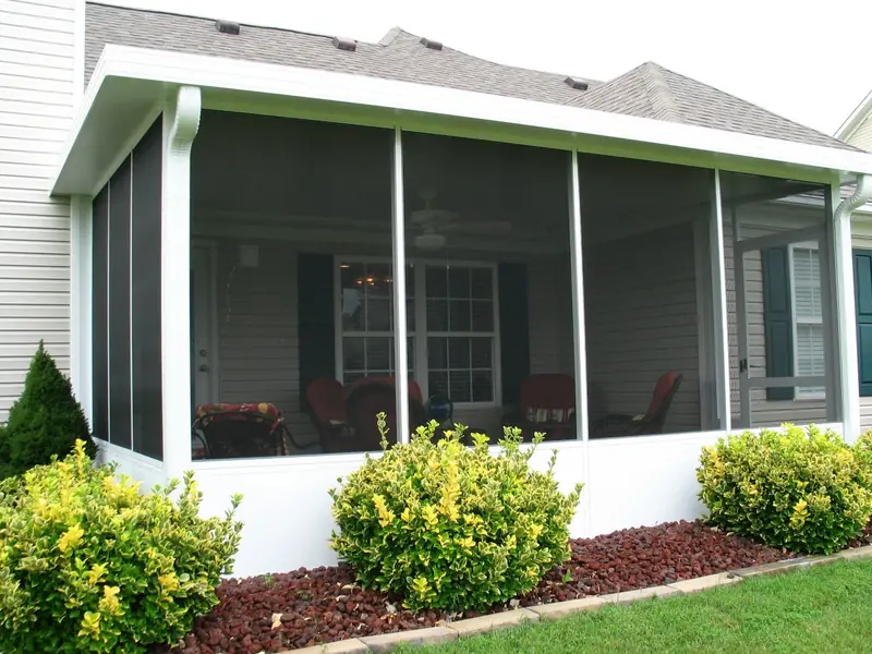 Screen room with white knee walls behind yellow flowering shrubs