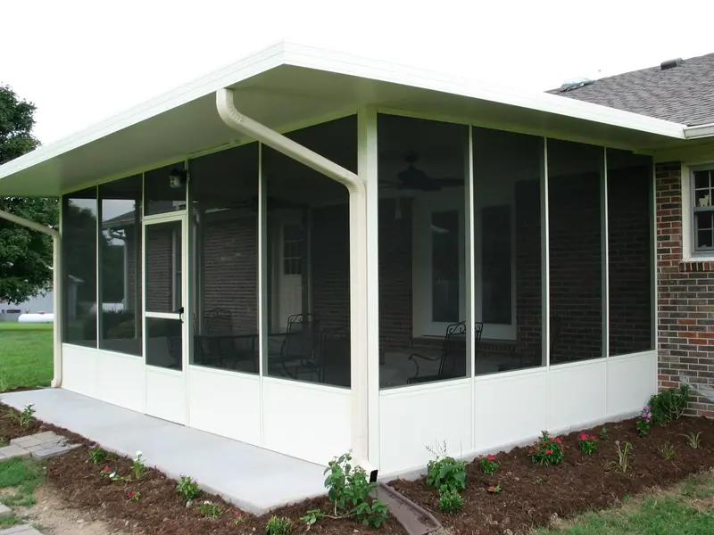 Screen room with an insulated aluminum roof and white knee walls beside a brick house