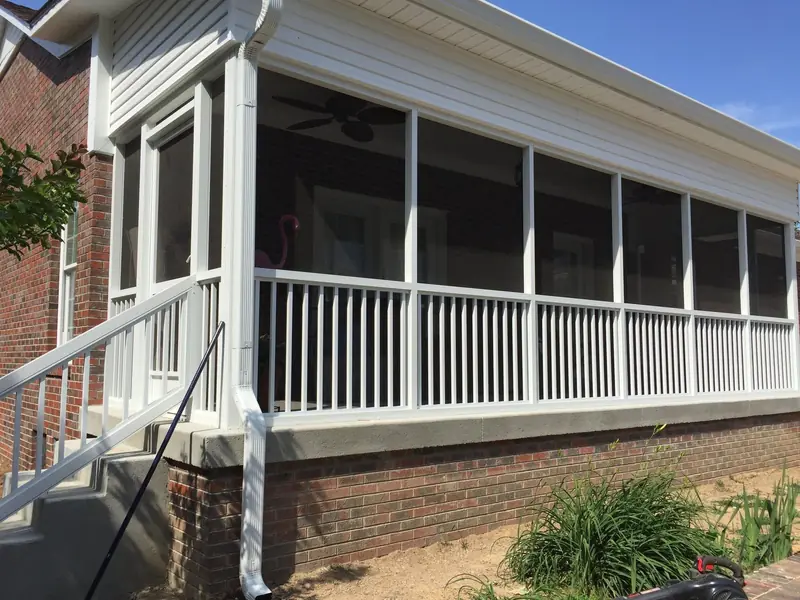 Long raised screen porch with white railing and steps on a brick home