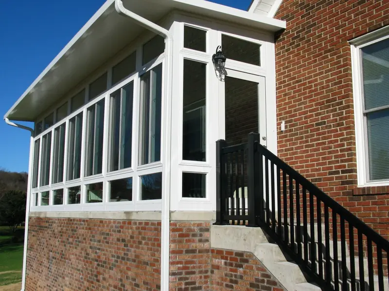 White glass sunroom with black stair railing on the side of a brick house