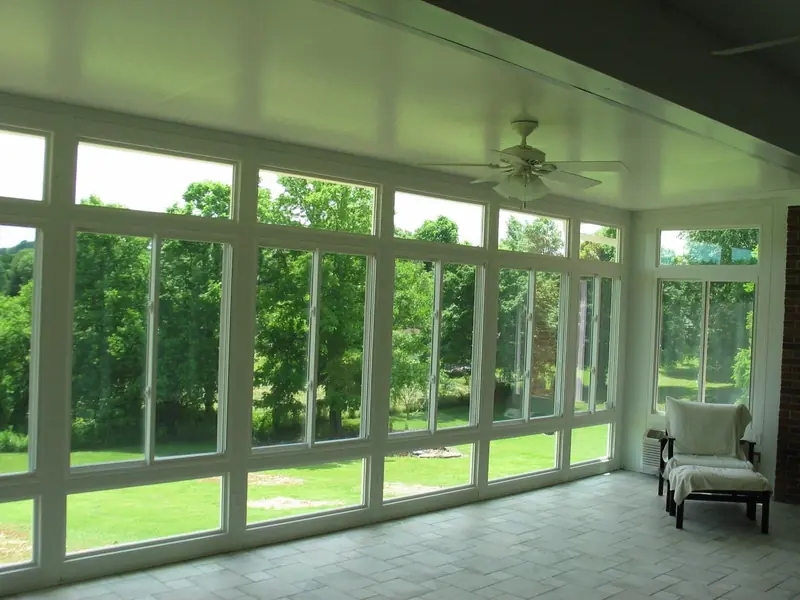 Bright sunroom interior with a ceiling fan, tile floor and a wall of windows facing the yard