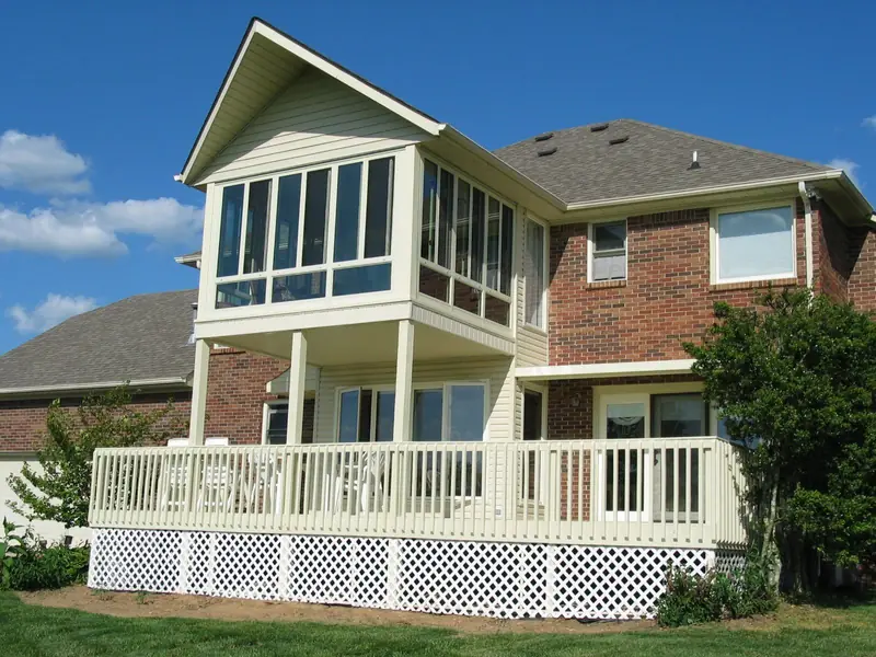 Second-story sunroom above a white deck on a large brick home