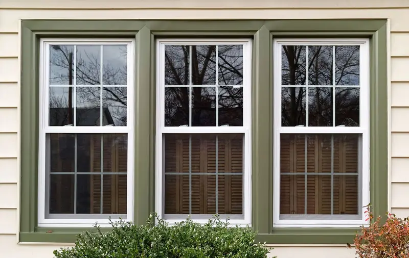 Three new double-hung replacement windows with grids on a home with green trim